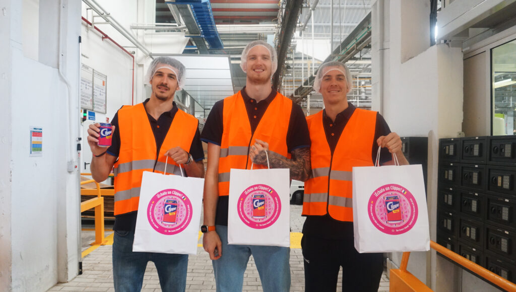  Nico Brussino y Olek Balcerowski visitan la fábrica de Ahembo",Jugadores en la fábrica de Ahembo sostienen bolsas y latas de producto.