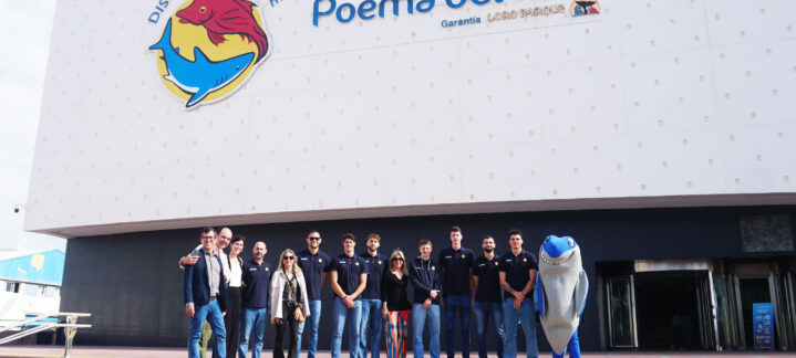 Grupo de personas en la entrada del acuario Poema del Mar, con un mascota de tiburón.