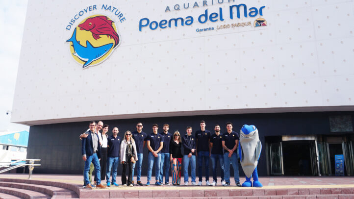 Grupo de personas en la entrada del acuario Poema del Mar, con un mascota de tiburón.