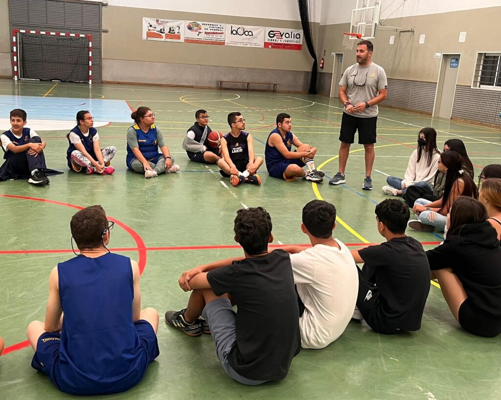 Cincuenta jóvenes participan en una sesión de baloncesto en un gimnasio.