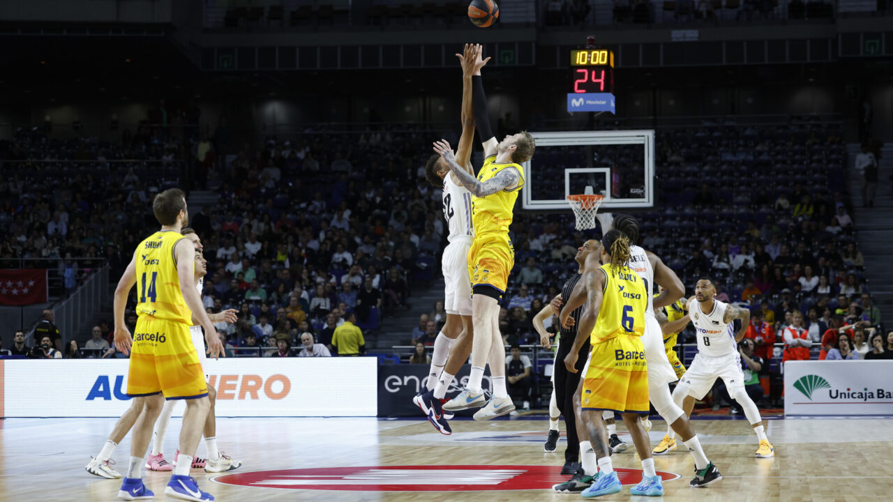 Jugadores saltando para el salto inicial en un partido de baloncesto en el Gran Canaria Arena.
