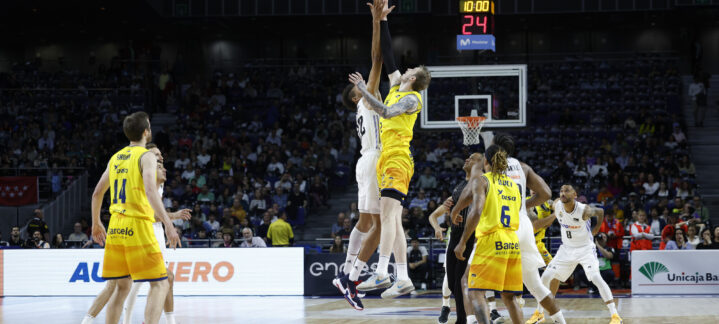 Jugadores saltando para el salto inicial en un partido de baloncesto en el Gran Canaria Arena.