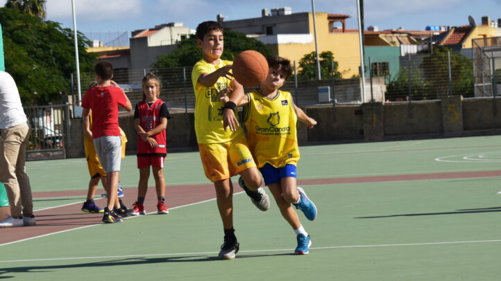 Niños jugando baloncesto en una cancha, lanzando y recibiendo un balón.