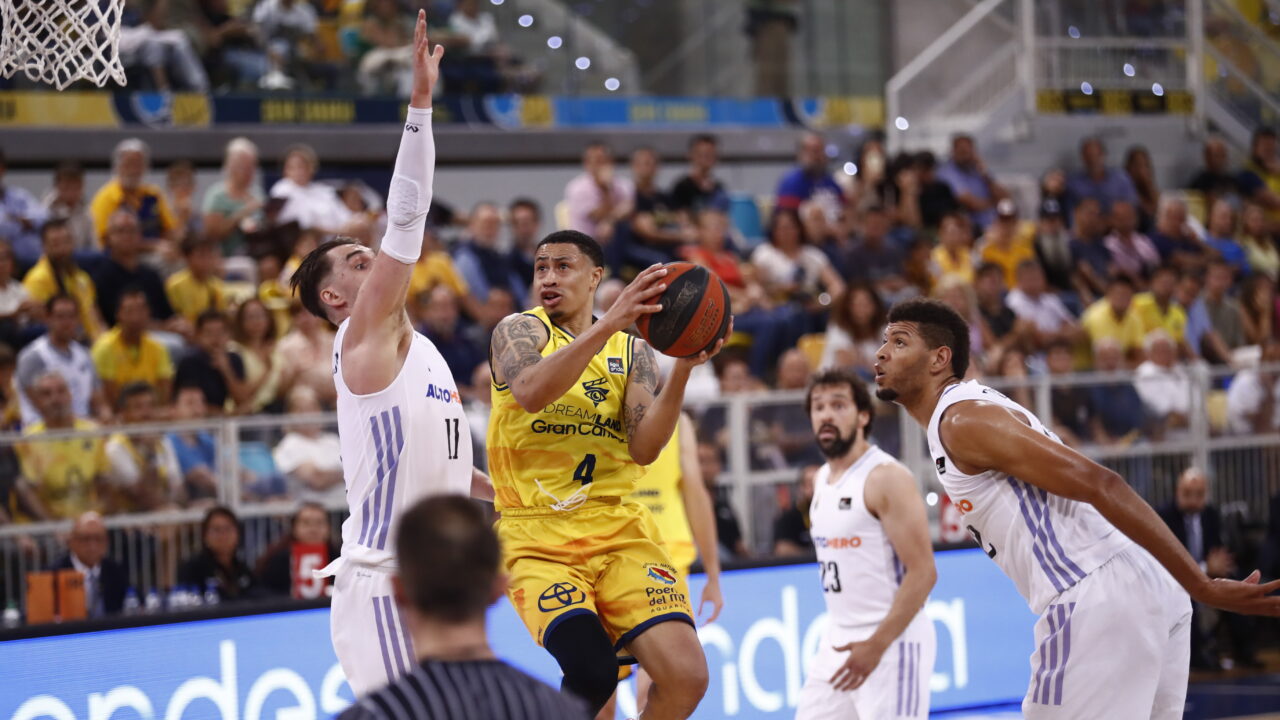 AJ Slaughter lanza a canasta mientras es defendido por jugadores rivales en un partido.