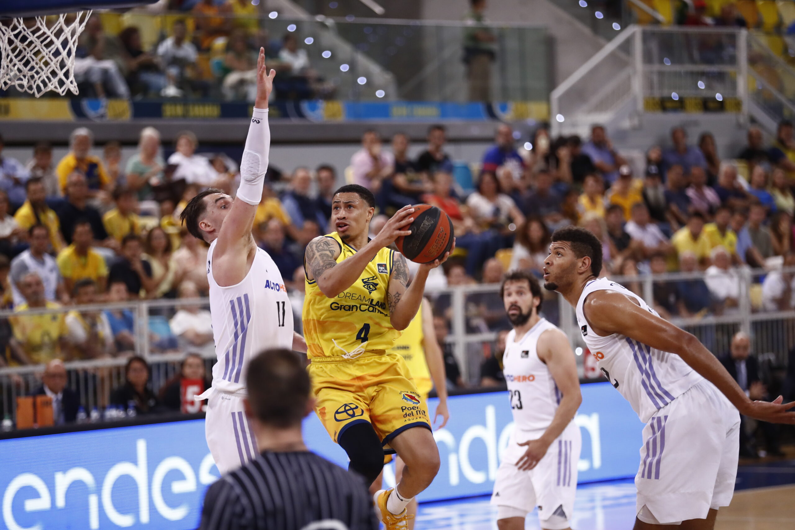 AJ Slaughter lanza a canasta mientras es defendido por jugadores rivales en un partido.