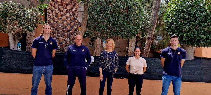 Grupo de personas en un evento al aire libre con plantas y pared de fondo.