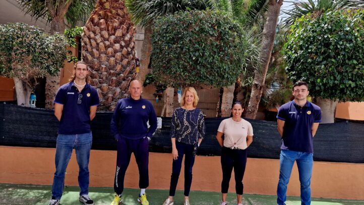 Grupo de personas en un evento al aire libre con plantas y pared de fondo.