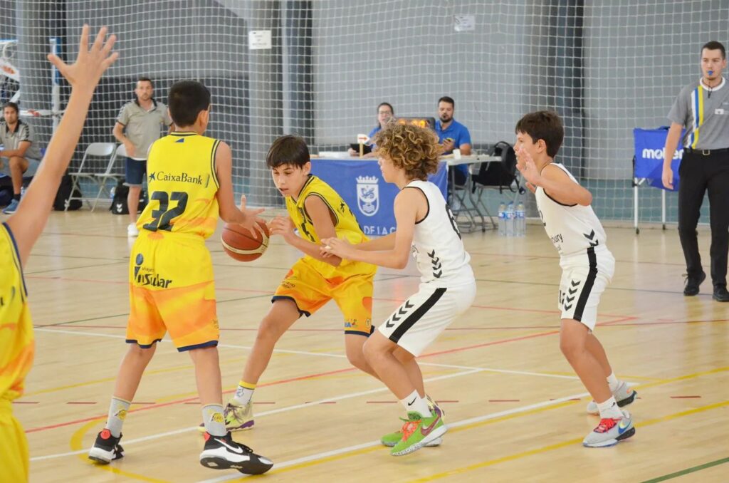 Jugadores de minibasket masculino compiten en un partido en una cancha interior.