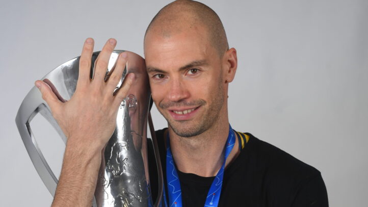 Oliver Stevic sostiene un trofeo, luciendo una medalla y sonriendo ante la cámara.