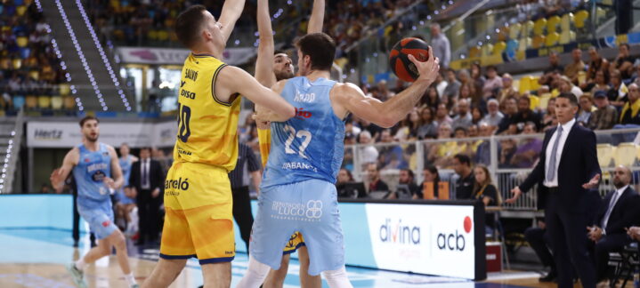 Jugadores en acción durante un partido de baloncesto, con público animando.