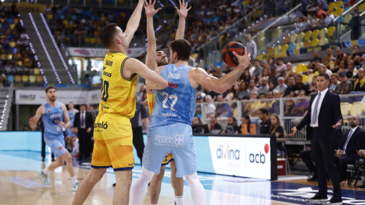 Jugadores en acción durante un partido de baloncesto, con público animando.