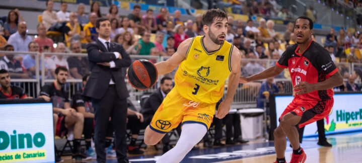 Jugador del Gran Canaria avanza con el balón mientras un oponente lo sigue de cerca.