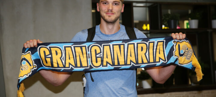 Jugador sostiene una bufanda del Club Baloncesto Gran Canaria, sonriendo emocionado.