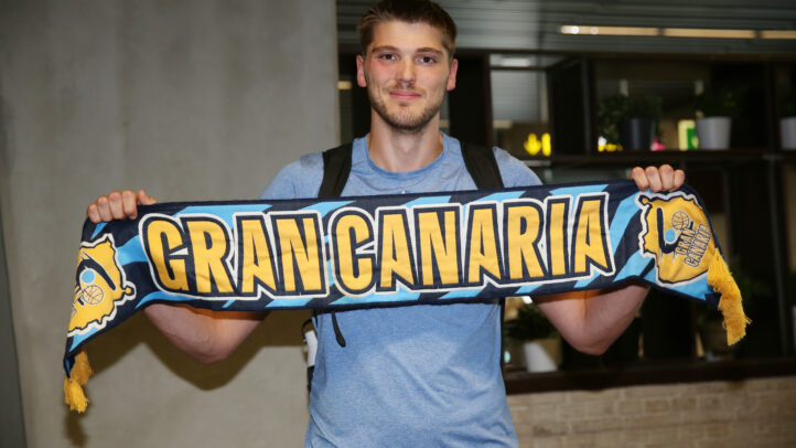 Jugador sostiene una bufanda del Club Baloncesto Gran Canaria, sonriendo emocionado.