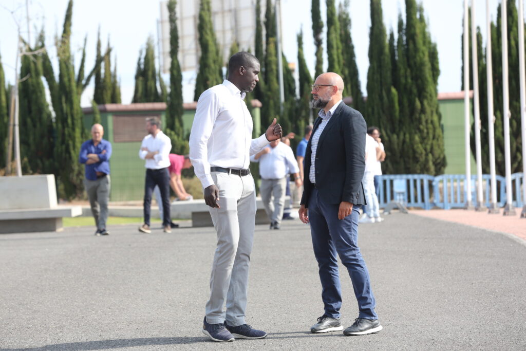 consejero de Deportes del Cabildo de Gran Canaria","Dos hombres conversan en el exterior del Club Baloncesto Gran Canaria, rodeados de árboles.