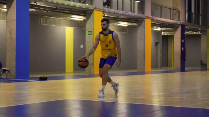 Jugador entrenando en cancha de baloncesto, driblando un balón con buena concentración.