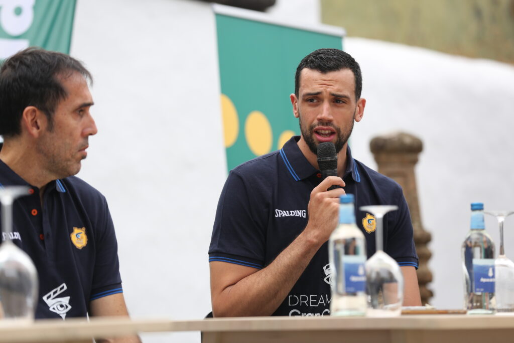 Pierre Pelos habla en la presentación junto a un compañero y botellas de agua.