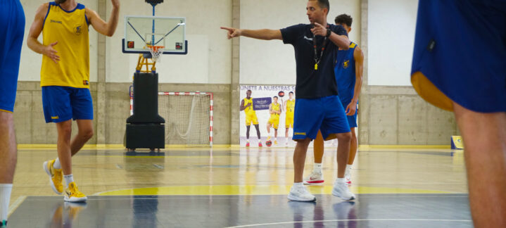 Entrenador dirige la práctica de baloncesto con jugadores en el campo.