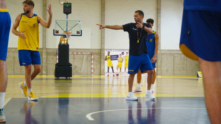Entrenador dirige la práctica de baloncesto con jugadores en el campo.