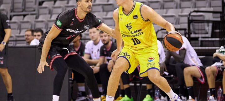 Dos jugadores de baloncesto en acción durante un partido, uno con balón y el otro defendiendo.