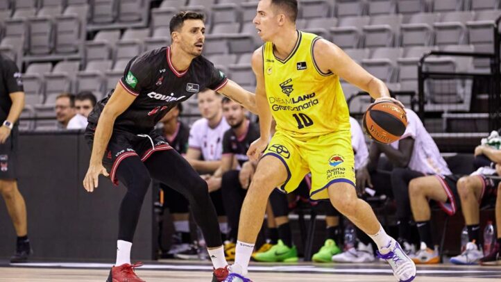 Dos jugadores de baloncesto en acción durante un partido, uno con balón y el otro defendiendo.