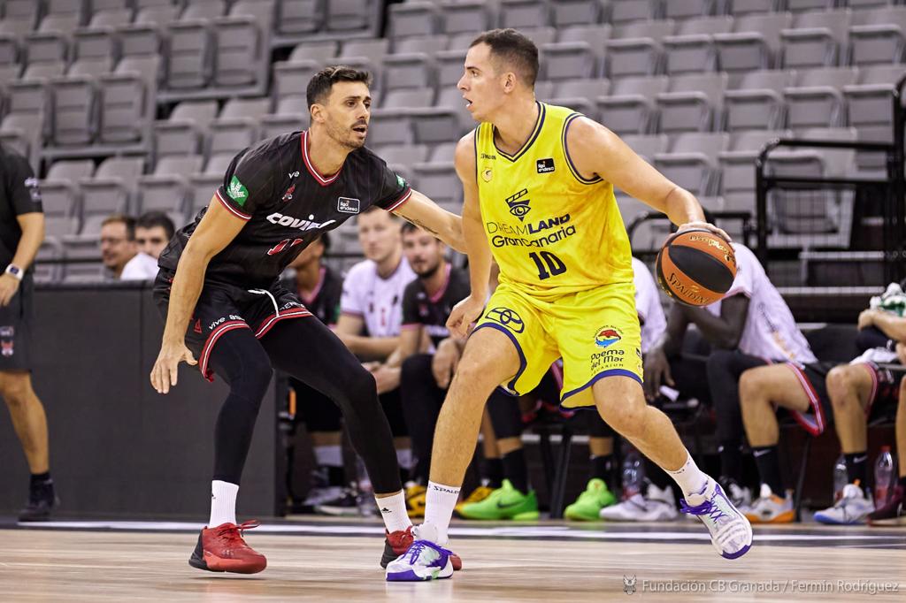 Dos jugadores de baloncesto en acción durante un partido, uno con balón y el otro defendiendo.