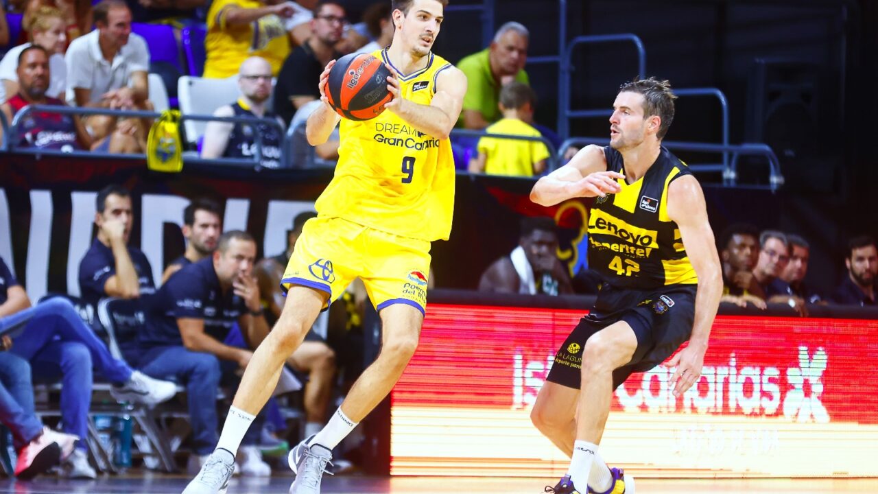 Jugador de baloncesto en acción durante un partido, lanzando el balón a otro compañero.