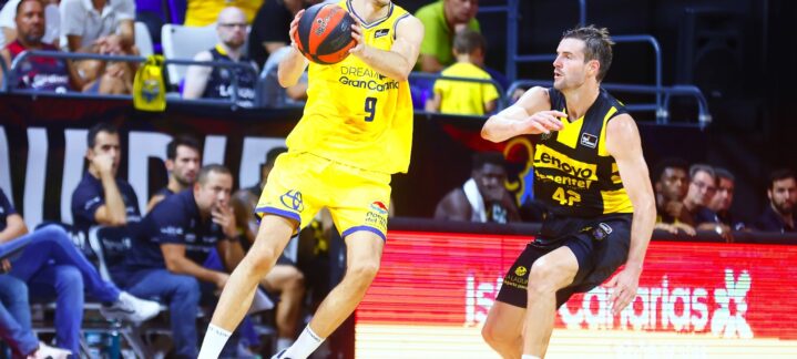 Jugador de baloncesto en acción durante un partido, lanzando el balón a otro compañero.