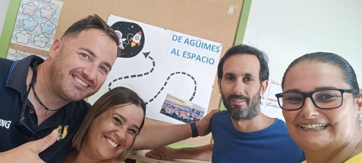 Cuatro personas sonrientes posan junto a un cartel del Proyecto Suma 5.0.