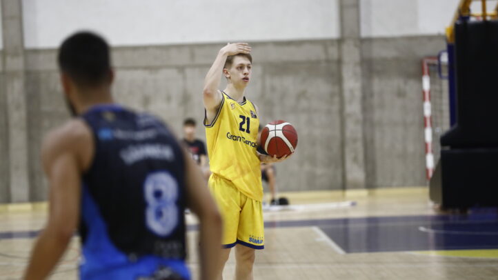 Jugadores de baloncesto en el campo, uno lanza con un balón en mano, luciendo uniforme amarillo.