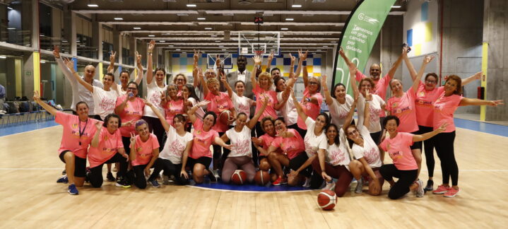 Participantes en un partido de baloncesto 'rosa' contra el cáncer de mama, sonriendo y animando.