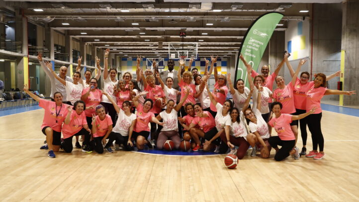 Participantes en un partido de baloncesto 'rosa' contra el cáncer de mama, sonriendo y animando.