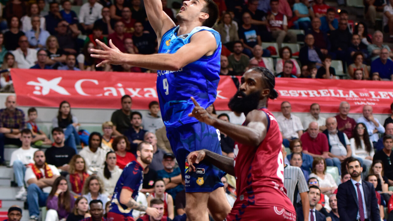 Jugadores en acción durante un partido de baloncesto. El equipo azul intenta anotar.