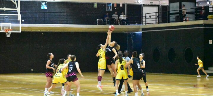 Jugadoras de baloncesto compiten en un salto para el rebote durante un partido.