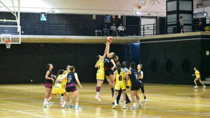 Jugadoras de baloncesto compiten en un salto para el rebote durante un partido.