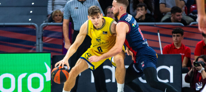 Jugador con balón intenta superar a un defensor en un partido de baloncesto.