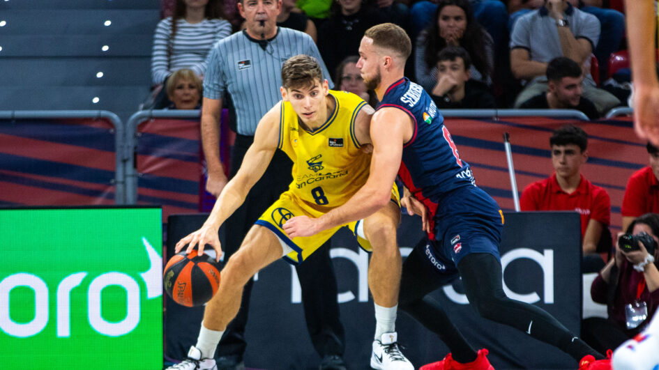 Jugador con balón intenta superar a un defensor en un partido de baloncesto.