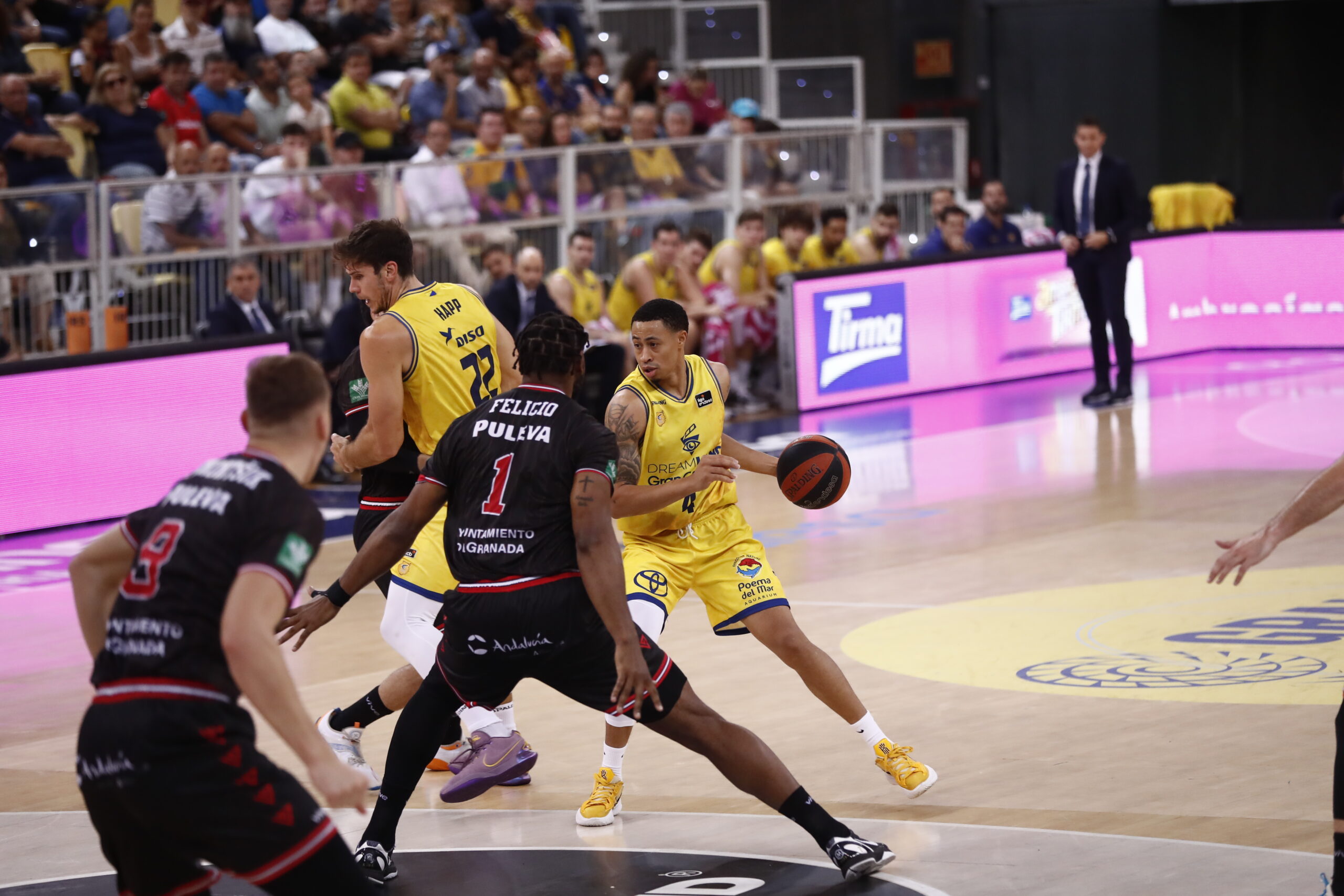 Jugadores en acción durante un partido de baloncesto, con público animando al fondo.