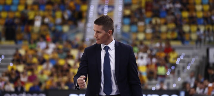 Entrenador Jaka Lakovic caminando por la pista durante un partido, con público al fondo.