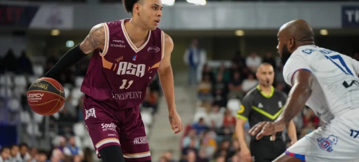 Jugador driblando el balón en un partido de baloncesto, enfrentándose a un oponente.