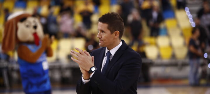Entrenador Jaka Lakovic aplaudiendo, con un mascota del club al fondo, en la cancha.