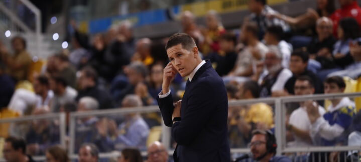 Entrenador en un partido de baloncesto, analizando la situación desde la línea de banda.
