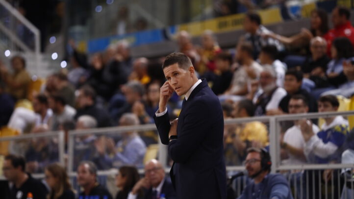 Entrenador en un partido de baloncesto, analizando la situación desde la línea de banda.