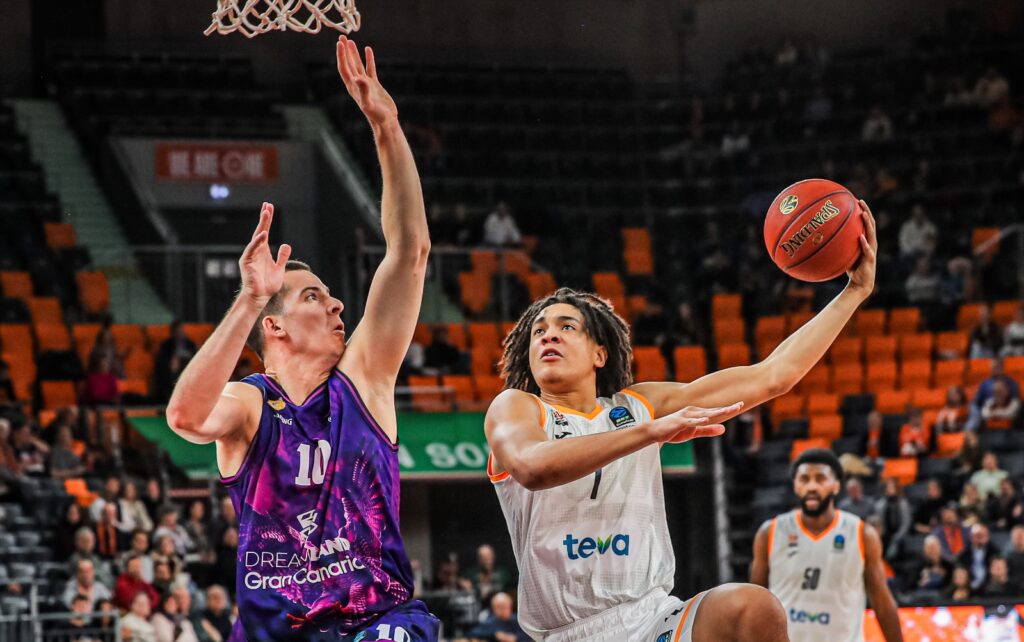 Dos jugadores de baloncesto compiten por un rebote en un partido emocionante.