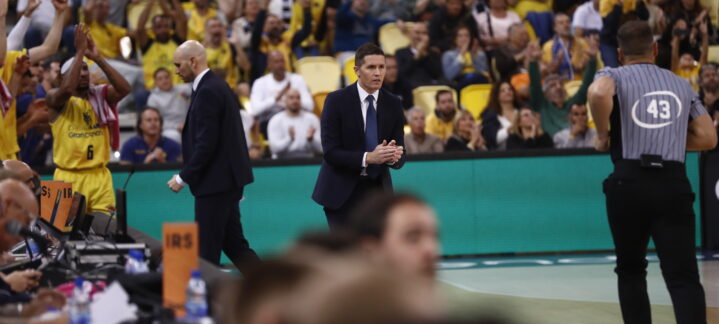 Entrenador Lakovic aplaudiendo con jugadores y afición animando en el fondo.