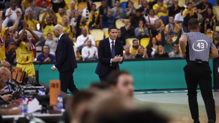 Entrenador Lakovic aplaudiendo con jugadores y afición animando en el fondo.
