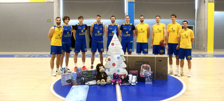 Jugadores del CB Gran Canaria presentan regalos junto a un árbol navideño en la pista.