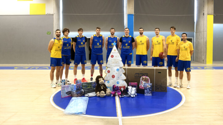 Jugadores del CB Gran Canaria presentan regalos junto a un árbol navideño en la pista.