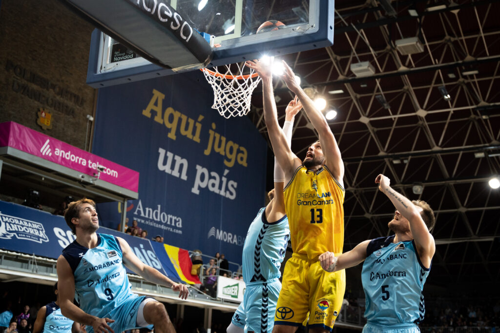 Jugadores en acción durante un partido de baloncesto, con una canasta en juego.
