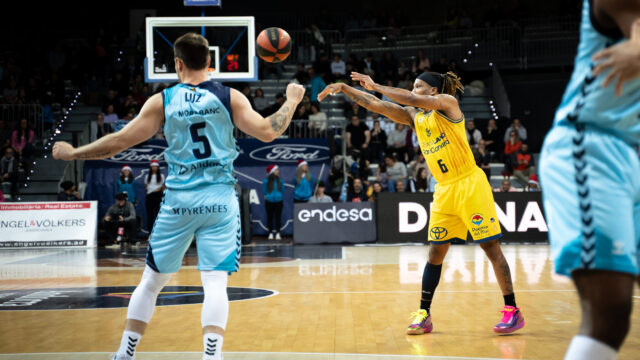 Jugador del Gran Canaria lanza el balón mientras el defensor observa en la cancha.